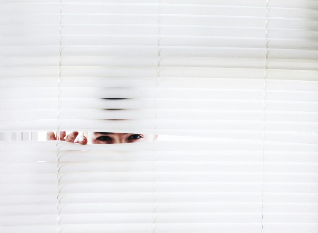 A person peeks through white blinds, creating an intriguing sense of curiosity.